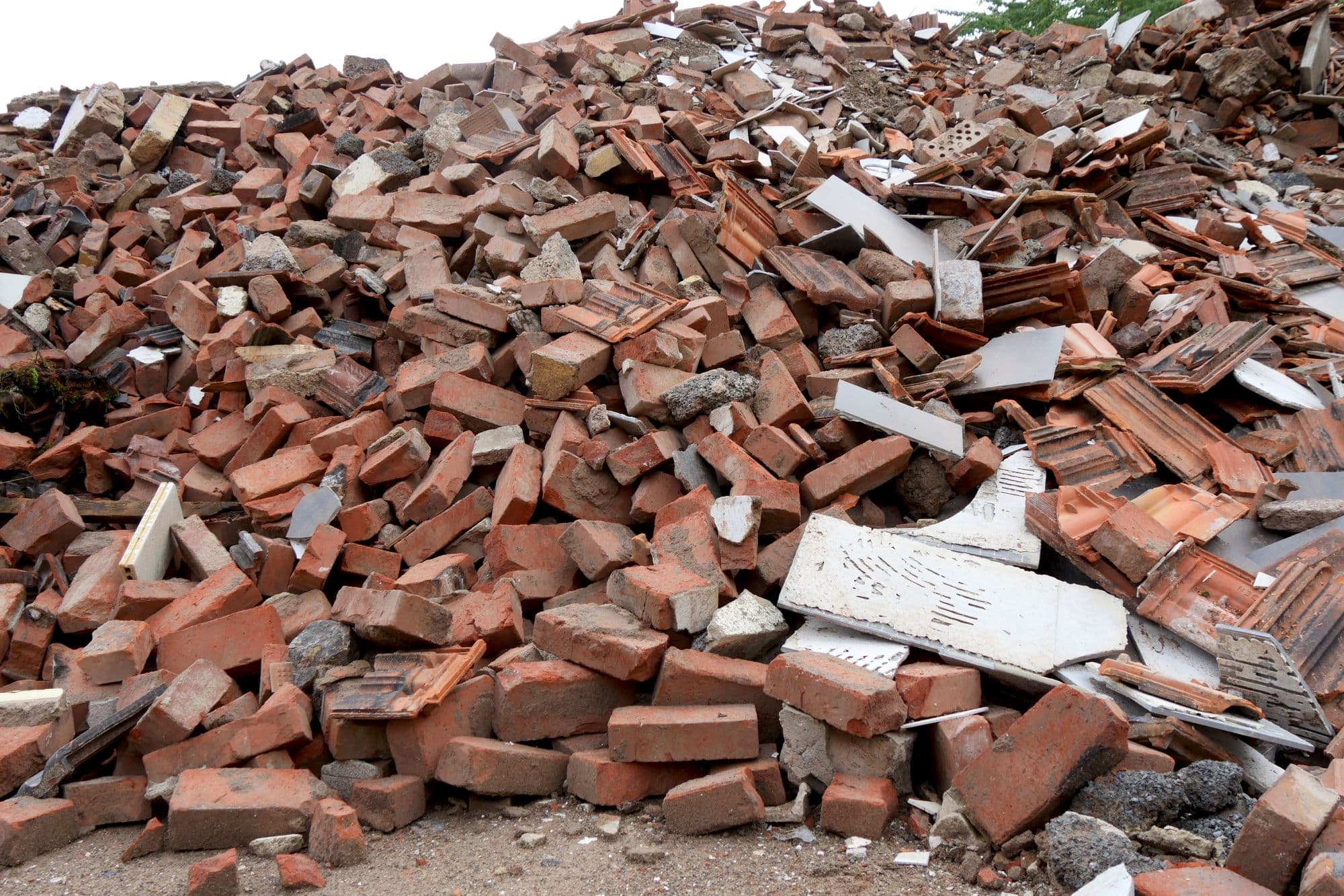 Large pile of red bricks, broken terracotta roof tiles, and concrete rubble from demolition.